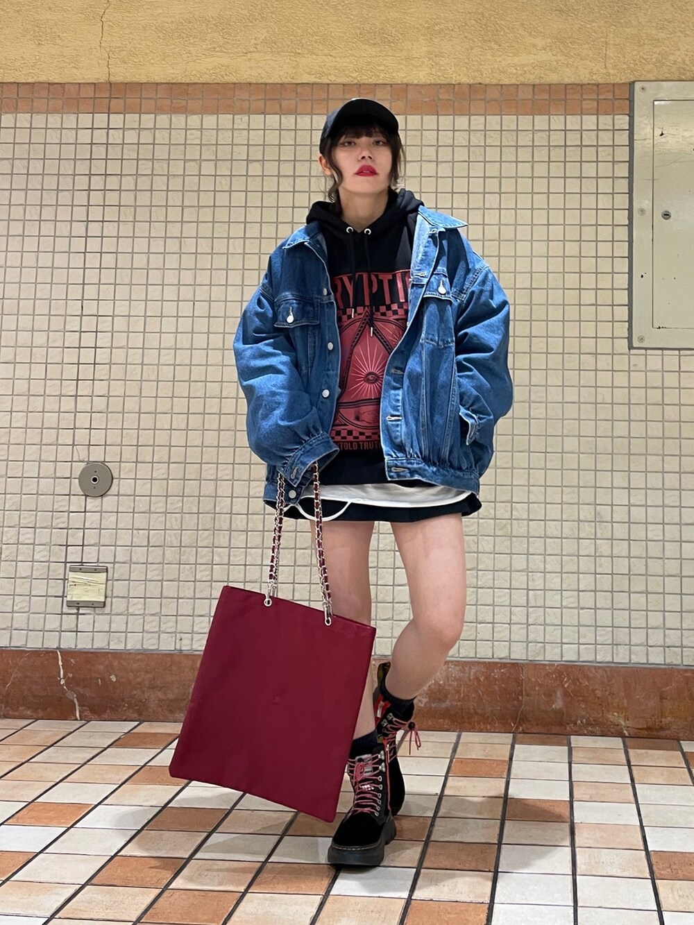 レッド系のトートバッグ、ブルー系のデニムジャケット、ブラック系のブーツを着用したレディースの冬コーディネートの2枚目の写真