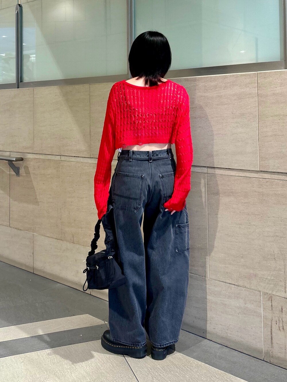 ブラック系のデニムパンツ、ブラック系のショルダーバッグ、レッド系のニット/セーターを着用したレディースの春コーディネートの4枚目の写真