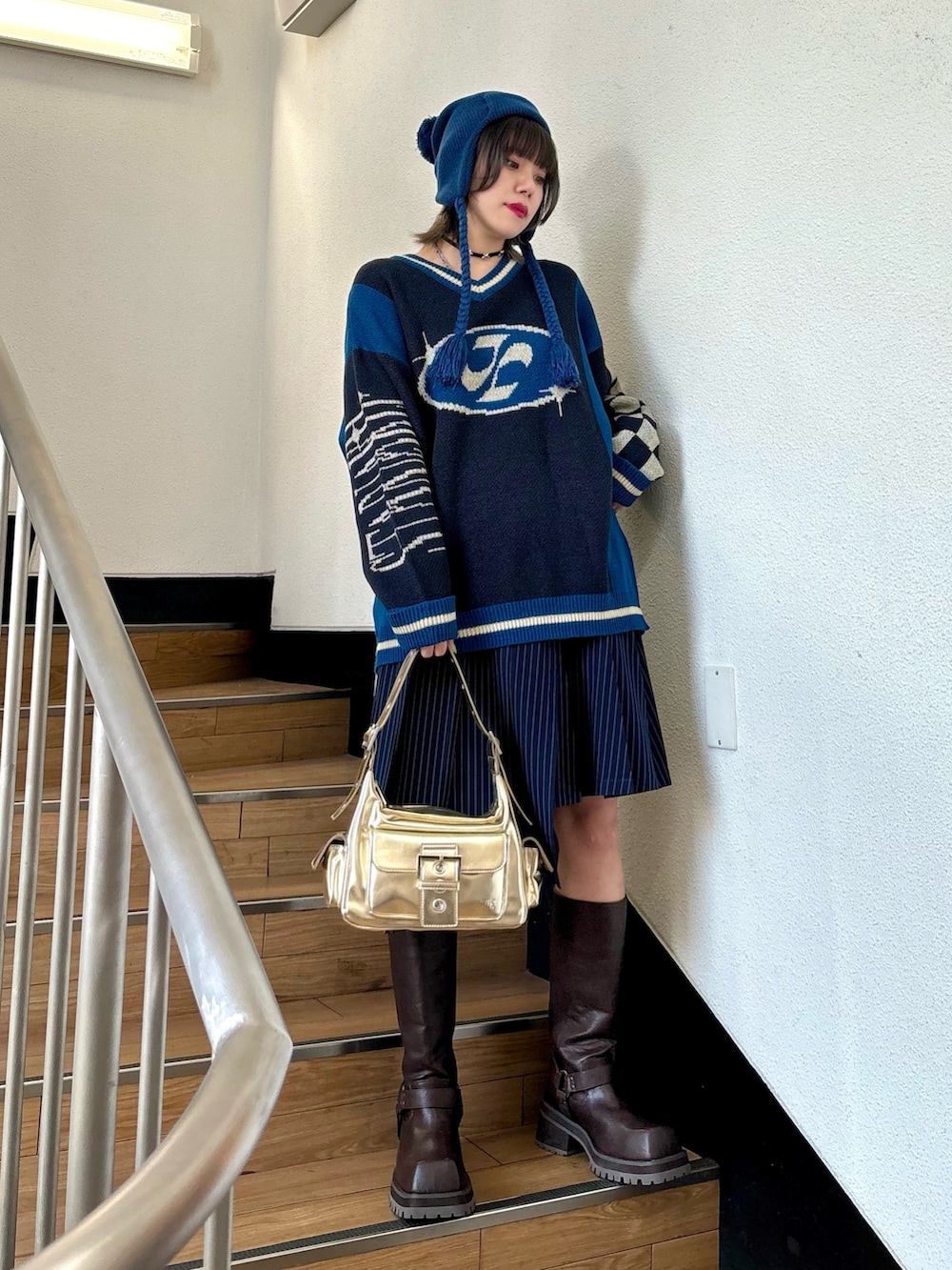 ブルー系のスカート、ゴールド系のハンドバッグ、ブラック系のニット/セーターを着用したレディースの夏コーディネートの2枚目の写真