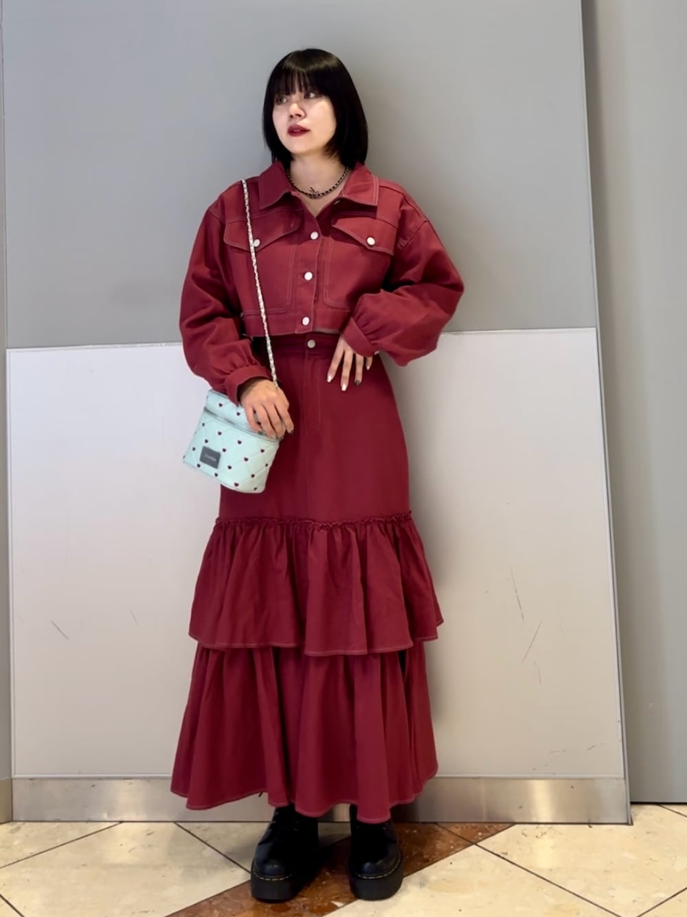 レッド系のワンピース、ブルー系のショルダーバッグ、ブラック系のネックレスを着用したレディースの秋コーディネートの2枚目の写真