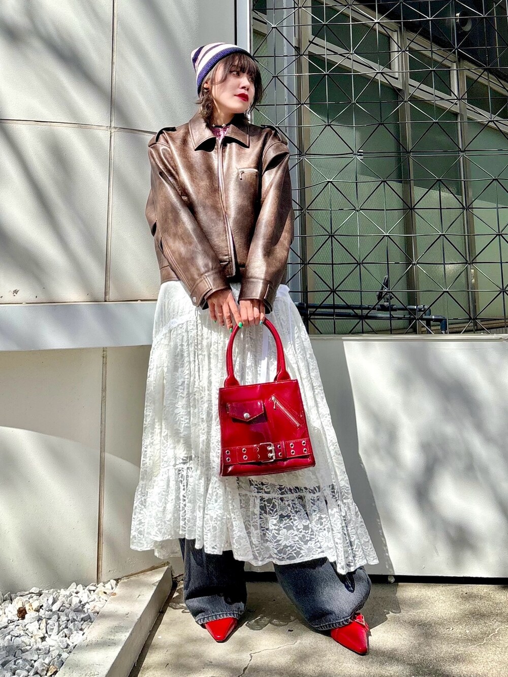 レッド系のハンドバッグ、レッド系のパンプス、ブラウン系のブルゾンを着用したレディースの夏コーディネートの2枚目の写真