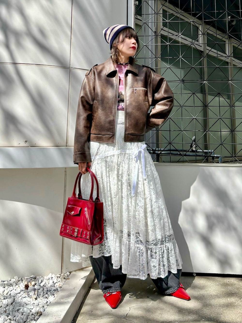 レッド系のハンドバッグ、レッド系のパンプス、ブラウン系のブルゾンを着用したレディースの夏コーディネートの3枚目の写真