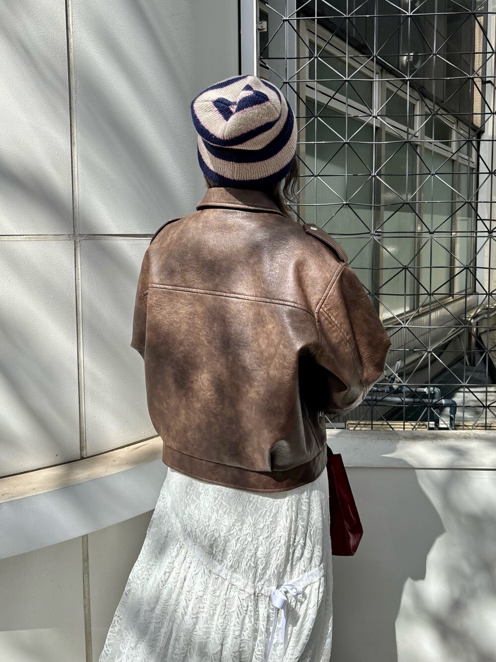 レッド系のハンドバッグ、レッド系のパンプス、ブラウン系のブルゾンを着用したレディースの夏コーディネートの5枚目の写真