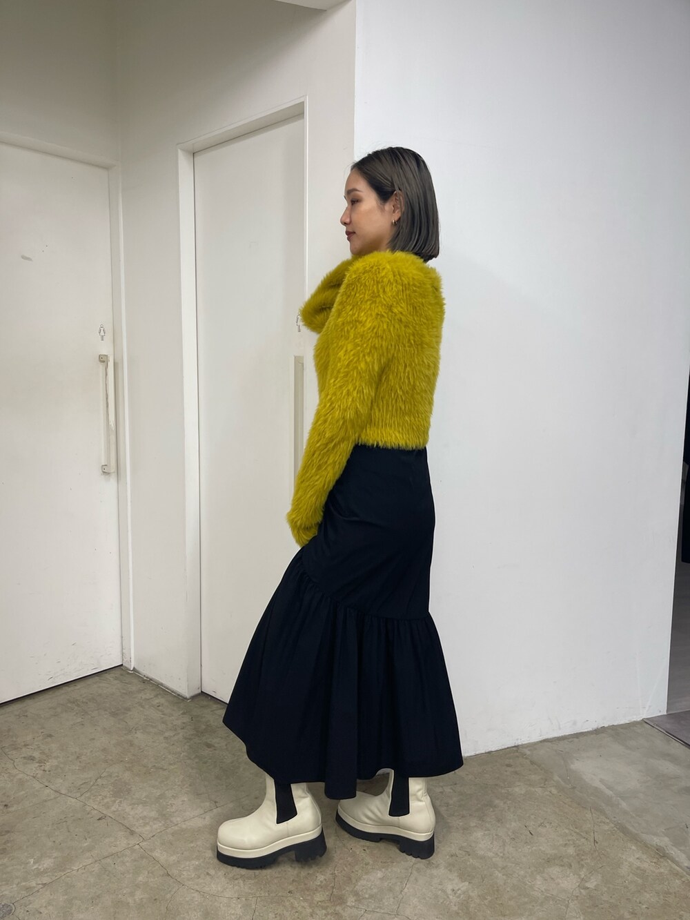 ブラック系のスカート、ホワイト系のブーツ、イエロー系のニット/セーターを着用したレディースの秋コーディネートの3枚目の写真