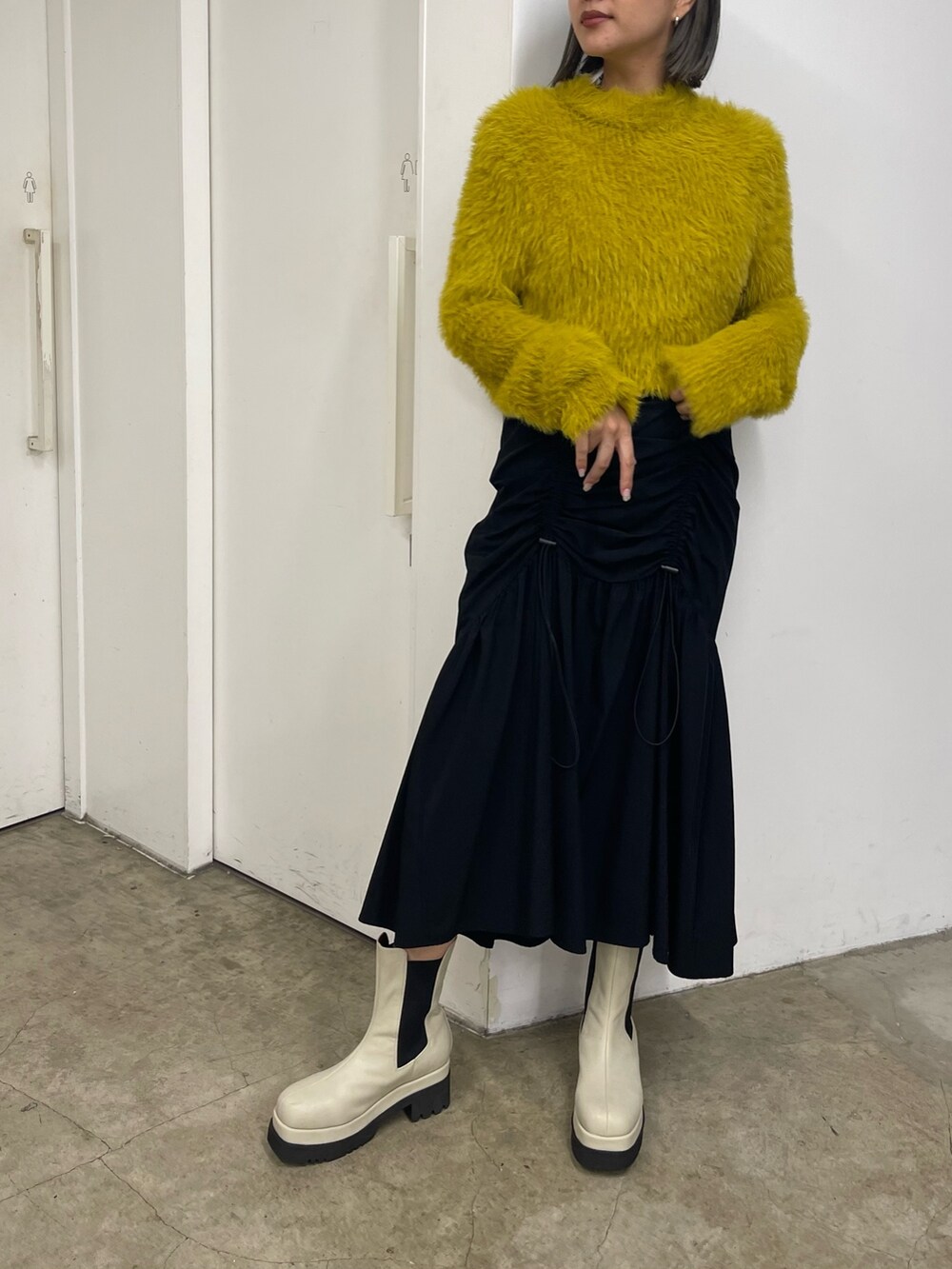 ブラック系のスカート、ホワイト系のブーツ、イエロー系のニット/セーターを着用したレディースの秋コーディネートの2枚目の写真