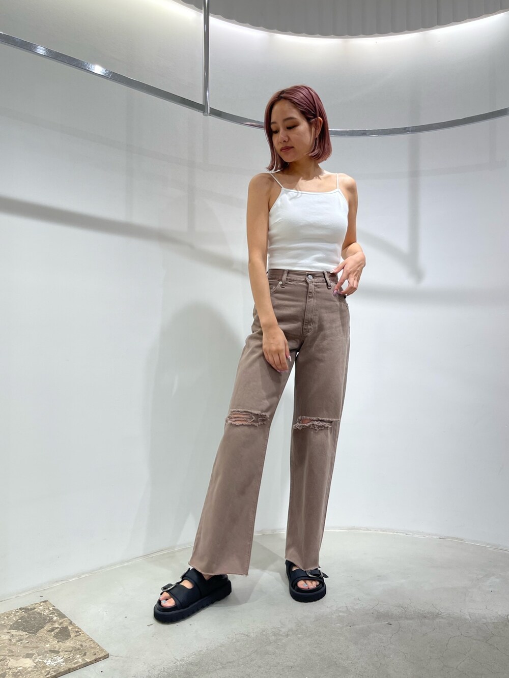 ブラック系のサンダル、ブラウン系のデニムパンツ、ホワイト系のキャミソールを着用したレディースの夏コーディネートの2枚目の写真