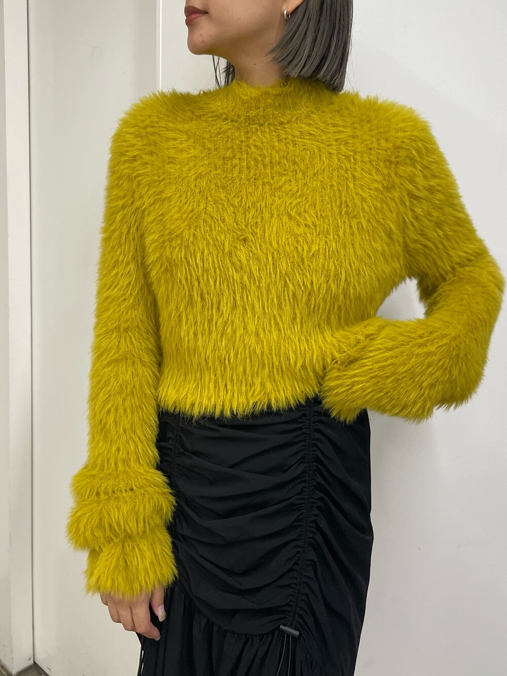 ブラック系のスカート、ホワイト系のブーツ、イエロー系のニット/セーターを着用したレディースの秋コーディネートの7枚目の写真