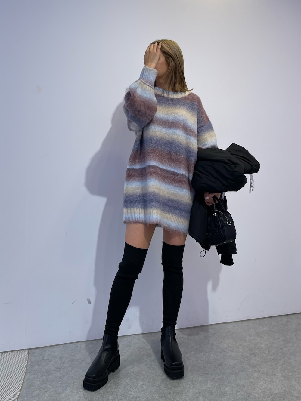 パープル系のニット/セーター、ブラック系のブーツ、ブラック系のダウンジャケット/コートを着用したレディースの冬コーディネートの2枚目の写真