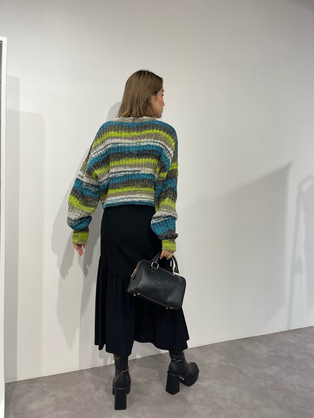 グリーン系のニット/セーター、ブラック系のボストンバッグ、ブラック系のスカートを着用したレディースの秋コーディネートの4枚目の写真