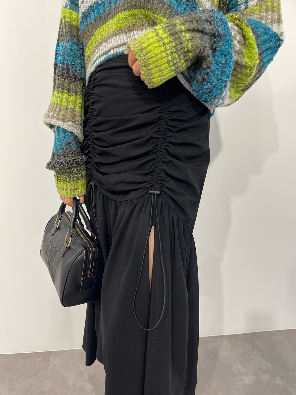 グリーン系のニット/セーター、ブラック系のボストンバッグ、ブラック系のスカートを着用したレディースの秋コーディネートの7枚目の写真