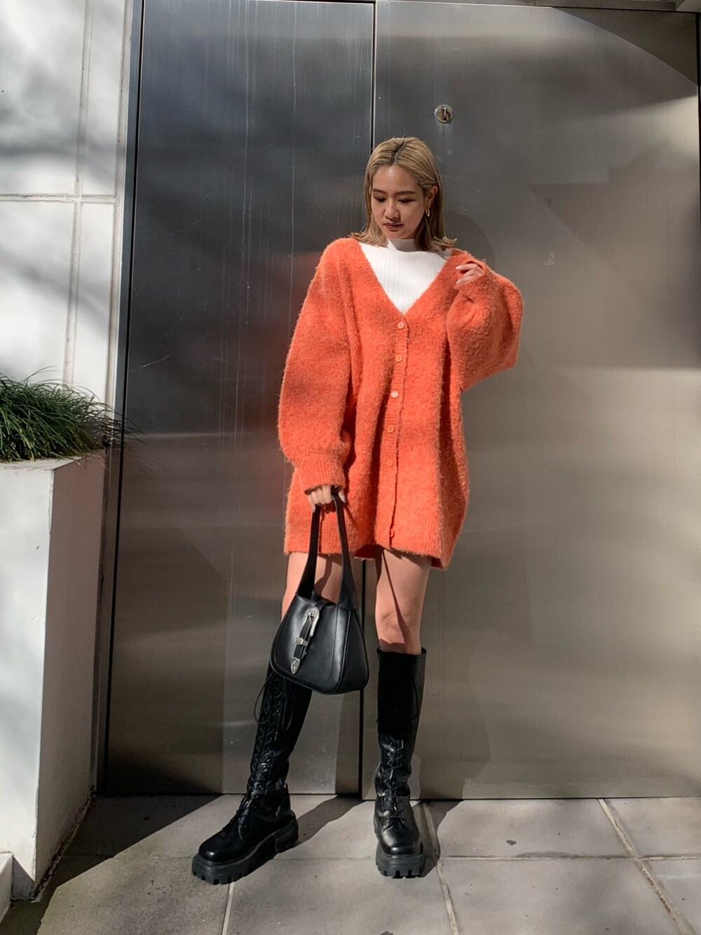 ブラック系のハンドバッグ、オレンジ系のカーディガン/ボレロ、ホワイト系のTシャツ/カットソーを着用したレディースの冬コーディネートの2枚目の写真