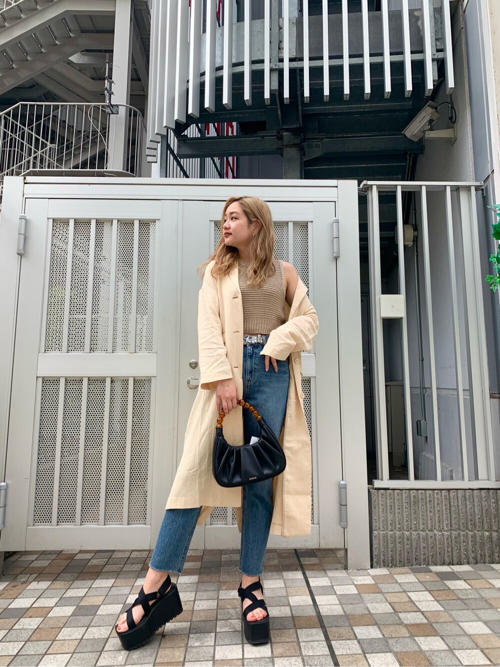 ブルー系のデニムパンツ、ブラック系のサンダル、ベージュ系のチェスターコートを着用したレディースの春コーディネートの2枚目の写真