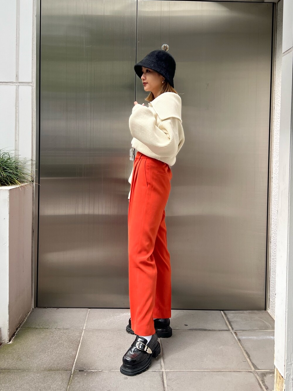 オレンジ系のスラックス、ホワイト系のニット/セーター、ブラック系のローファーを着用したレディースの秋コーディネートの3枚目の写真