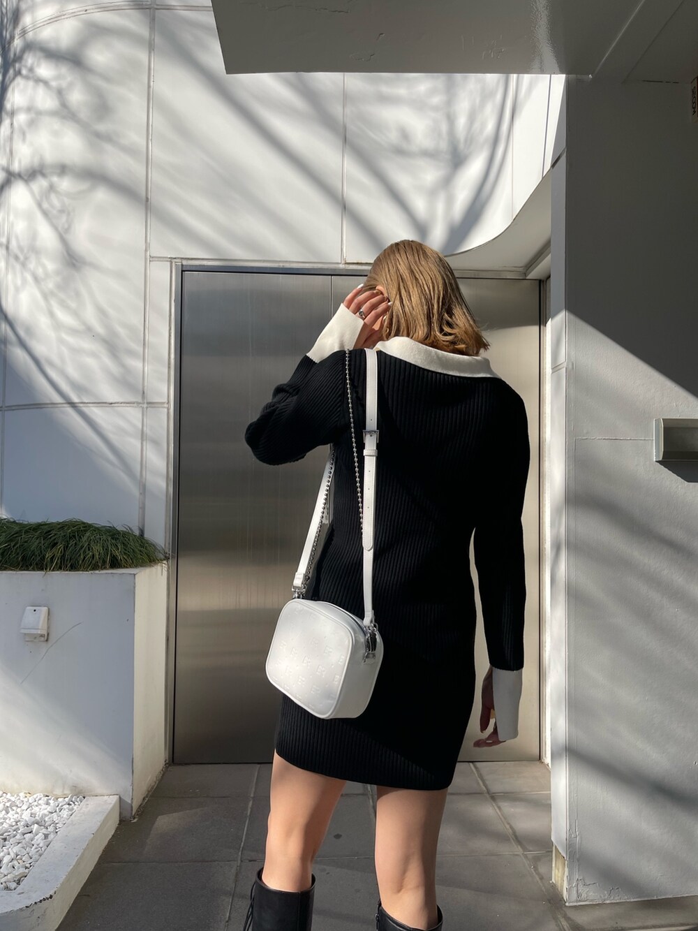 ブラック系のブーツ、ブラック系のワンピース、ホワイト系のショルダーバッグを着用したレディースの冬コーディネートの5枚目の写真