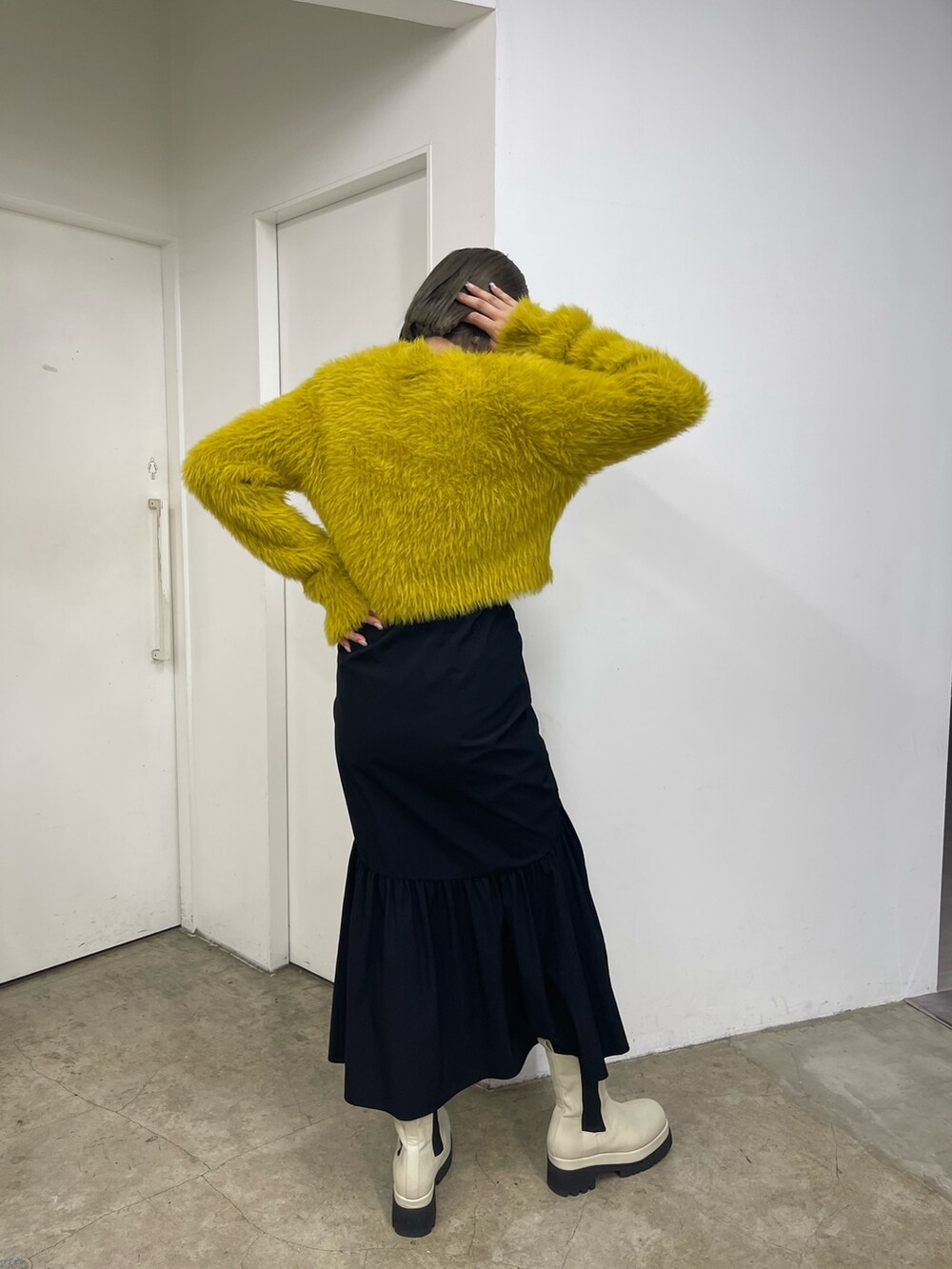 ブラック系のスカート、ホワイト系のブーツ、イエロー系のニット/セーターを着用したレディースの秋コーディネートの5枚目の写真