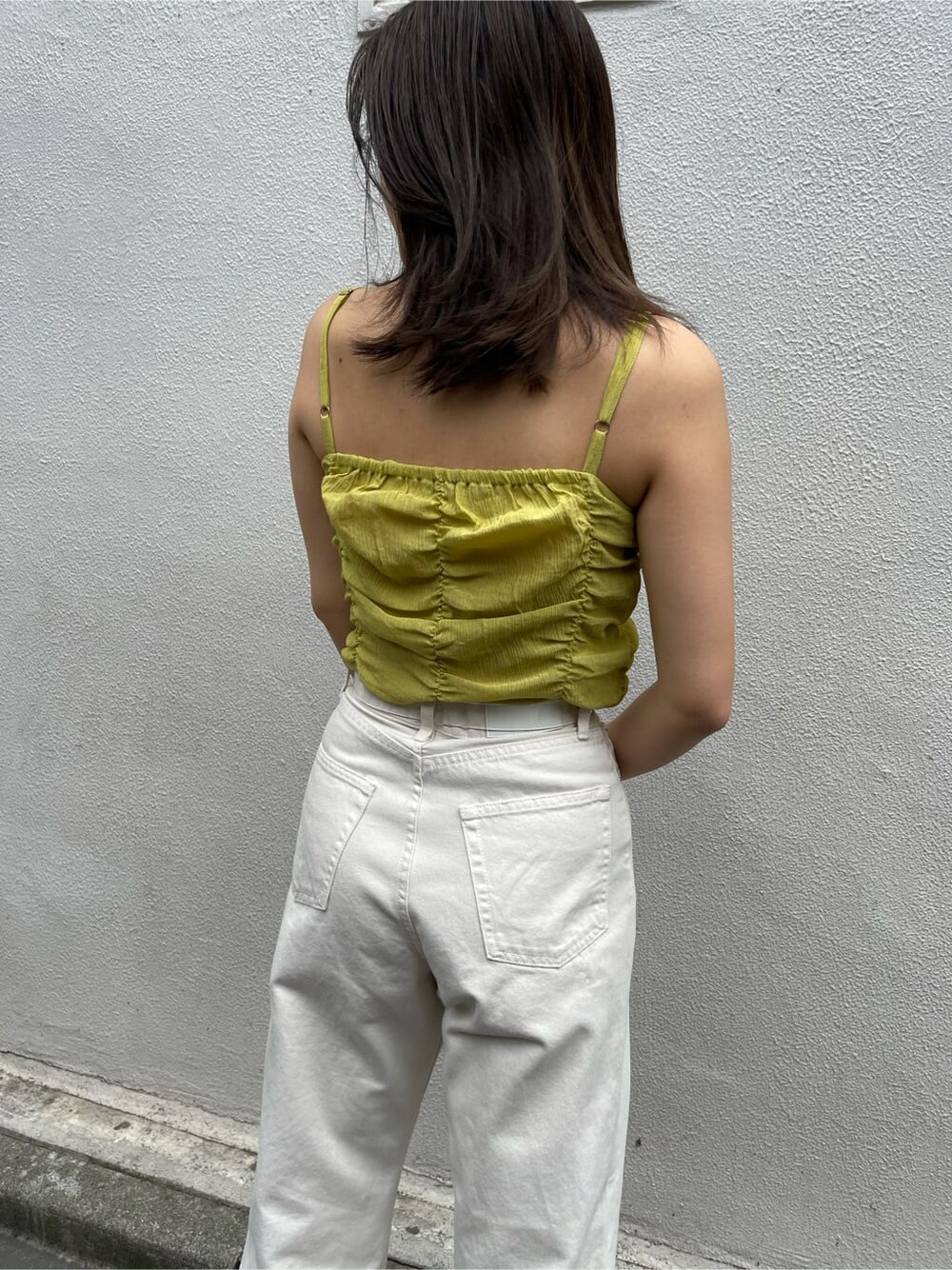 イエロー系のキャミソール、ホワイト系のデニムパンツ、ブラック系のサンダルを着用したレディースの夏コーディネートの4枚目の写真