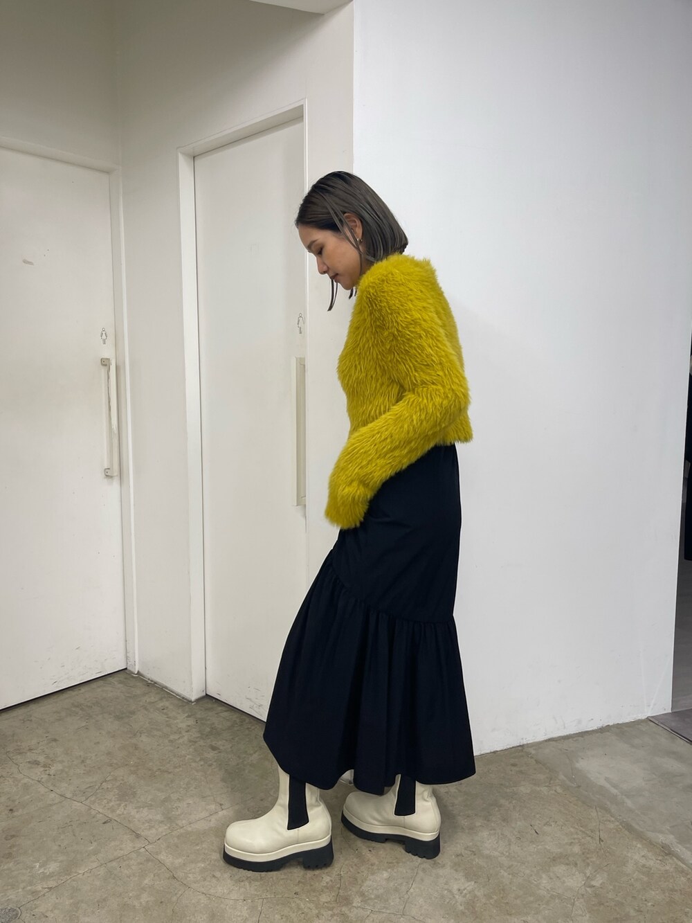 ブラック系のスカート、ホワイト系のブーツ、イエロー系のニット/セーターを着用したレディースの秋コーディネートの4枚目の写真