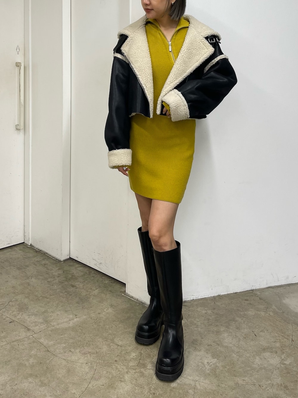 イエロー系のワンピース、ブラック系のブーツ、ブラック系のムートンコートを着用したレディースの秋コーディネートの3枚目の写真