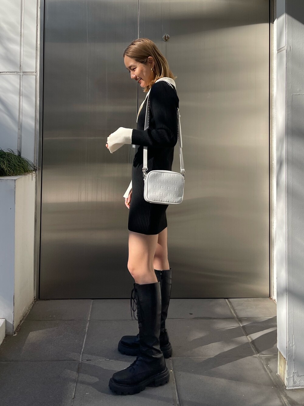 ブラック系のブーツ、ブラック系のワンピース、ホワイト系のショルダーバッグを着用したレディースの冬コーディネートの2枚目の写真