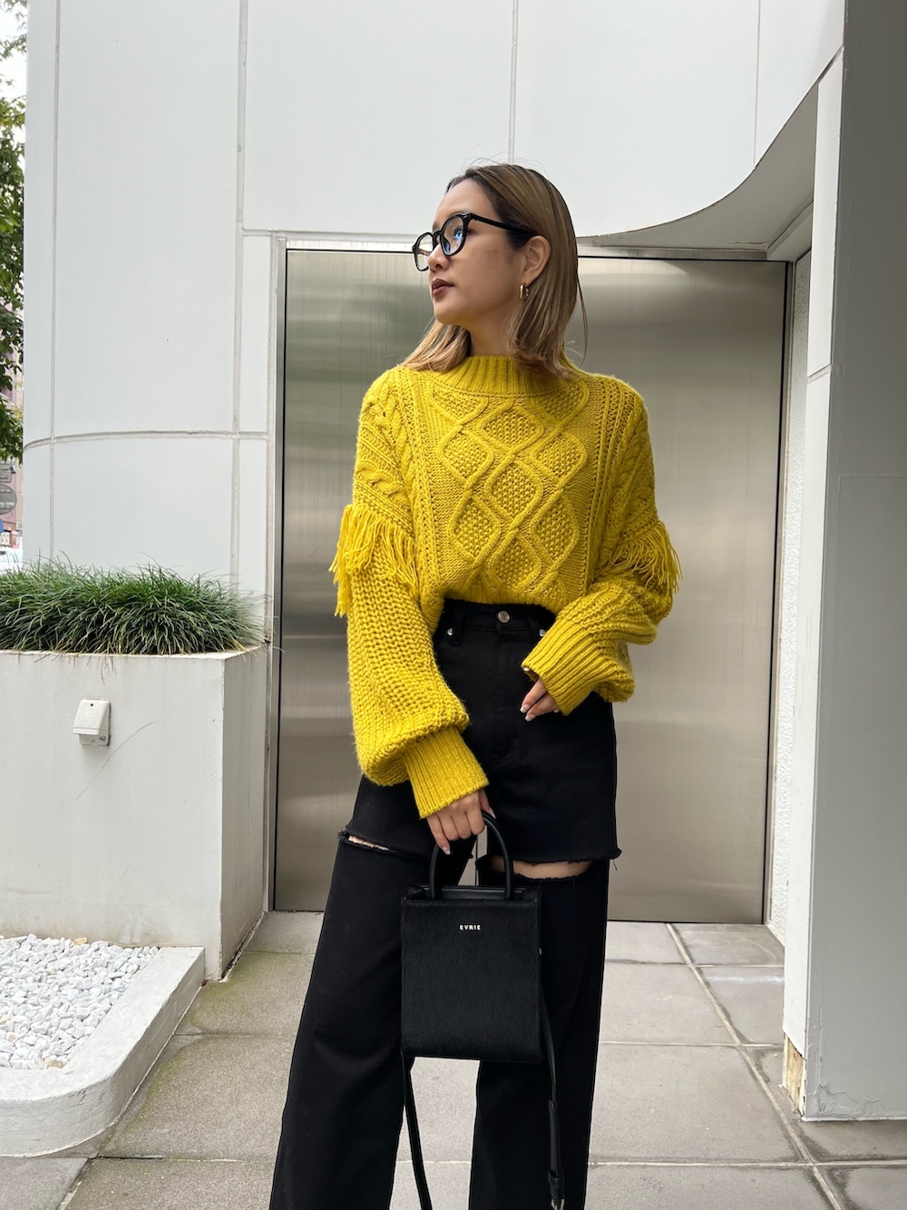 ブラック系のショルダーバッグ、イエロー系のニット/セーター、ブラック系のデニムパンツを着用したレディースの秋コーディネートの5枚目の写真