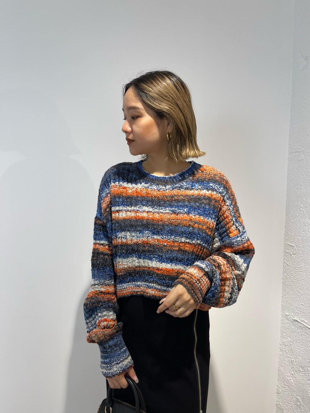 ブラック系のスカート、ブラック系のショルダーバッグ、オレンジ系のニット/セーターを着用したレディースの秋コーディネートの4枚目の写真