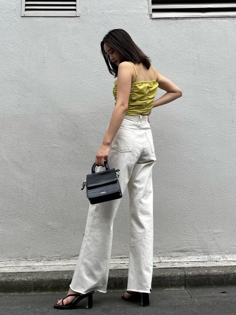 イエロー系のキャミソール、ホワイト系のデニムパンツ、ブラック系のサンダルを着用したレディースの夏コーディネートの2枚目の写真