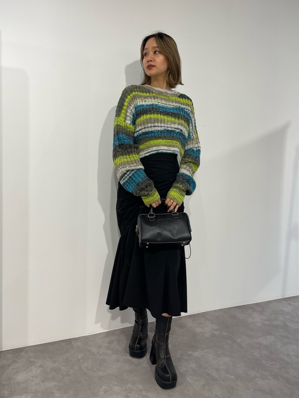 グリーン系のニット/セーター、ブラック系のボストンバッグ、ブラック系のスカートを着用したレディースの秋コーディネートの2枚目の写真