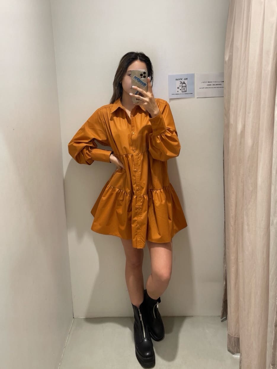 オレンジ系のシャツワンピース、ブラック系のブーツ、ブラック系のショルダーバッグを着用したレディースの冬コーディネートの2枚目の写真