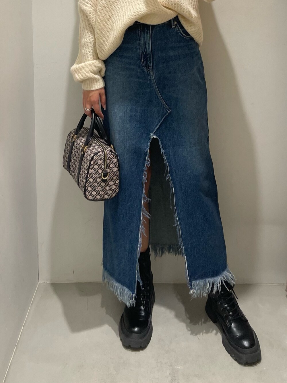 ブルー系のデニムスカート、ホワイト系のニット/セーター、ブラック系のブーツを着用したレディースの秋コーディネートの4枚目の写真