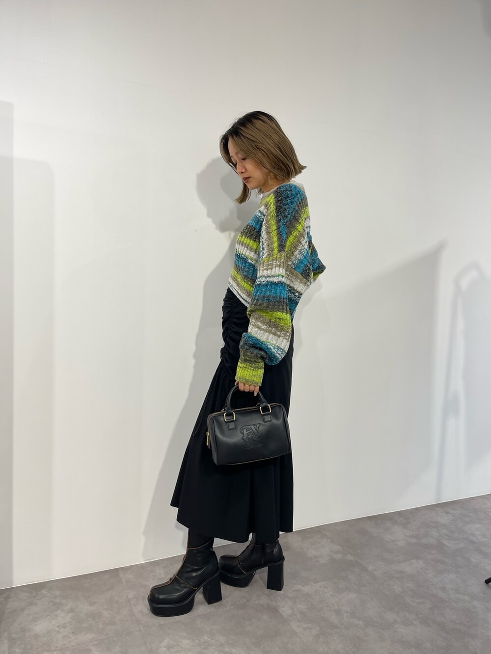 グリーン系のニット/セーター、ブラック系のボストンバッグ、ブラック系のスカートを着用したレディースの秋コーディネートの3枚目の写真