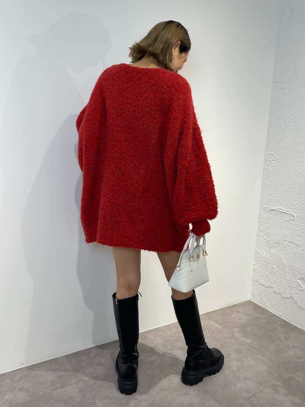 レッド系のニット/セーター、ブラック系のブーツ、ホワイト系のショルダーバッグを着用したレディースの秋コーディネートの3枚目の写真