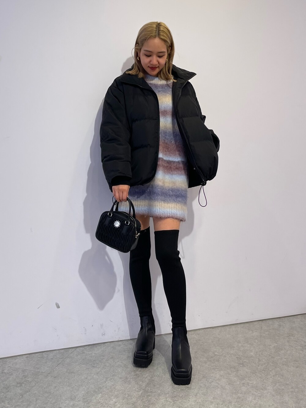 パープル系のニット/セーター、ブラック系のブーツ、ブラック系のダウンジャケット/コートを着用したレディースの冬コーディネートの3枚目の写真