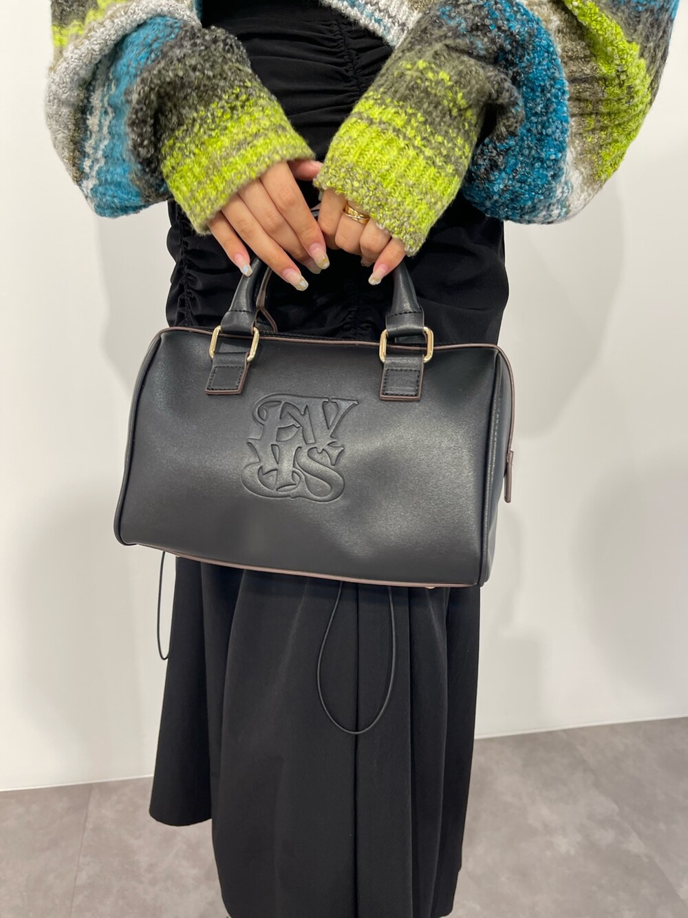 グリーン系のニット/セーター、ブラック系のボストンバッグ、ブラック系のスカートを着用したレディースの秋コーディネートの8枚目の写真