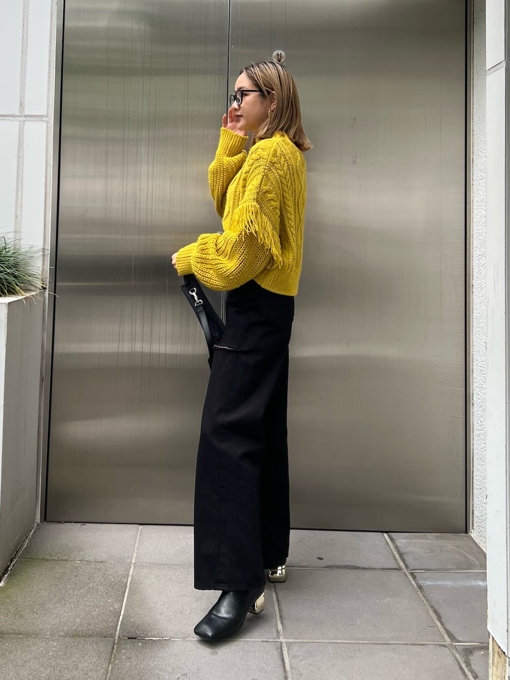 ブラック系のショルダーバッグ、イエロー系のニット/セーター、ブラック系のデニムパンツを着用したレディースの秋コーディネートの2枚目の写真