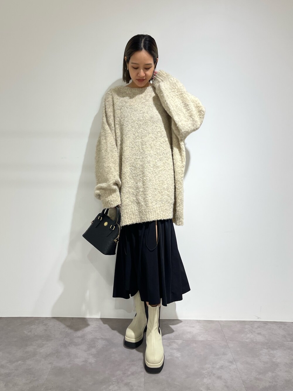 ブラック系のスカート、ホワイト系のブーツ、ブラック系のショルダーバッグを着用したレディースの秋コーディネートの2枚目の写真