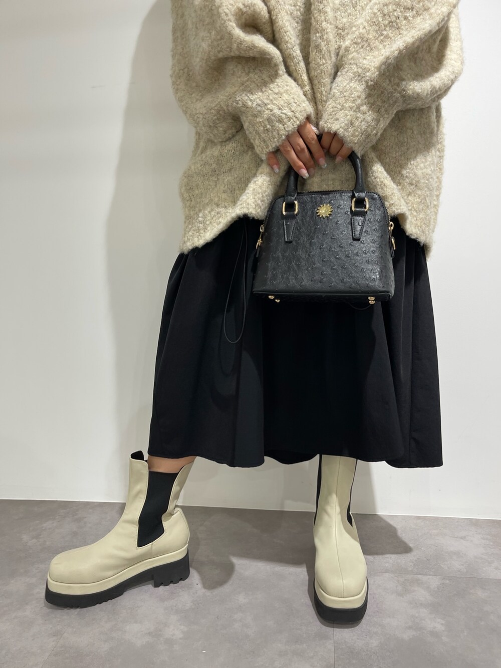 ブラック系のスカート、ホワイト系のブーツ、ブラック系のショルダーバッグを着用したレディースの秋コーディネートの7枚目の写真