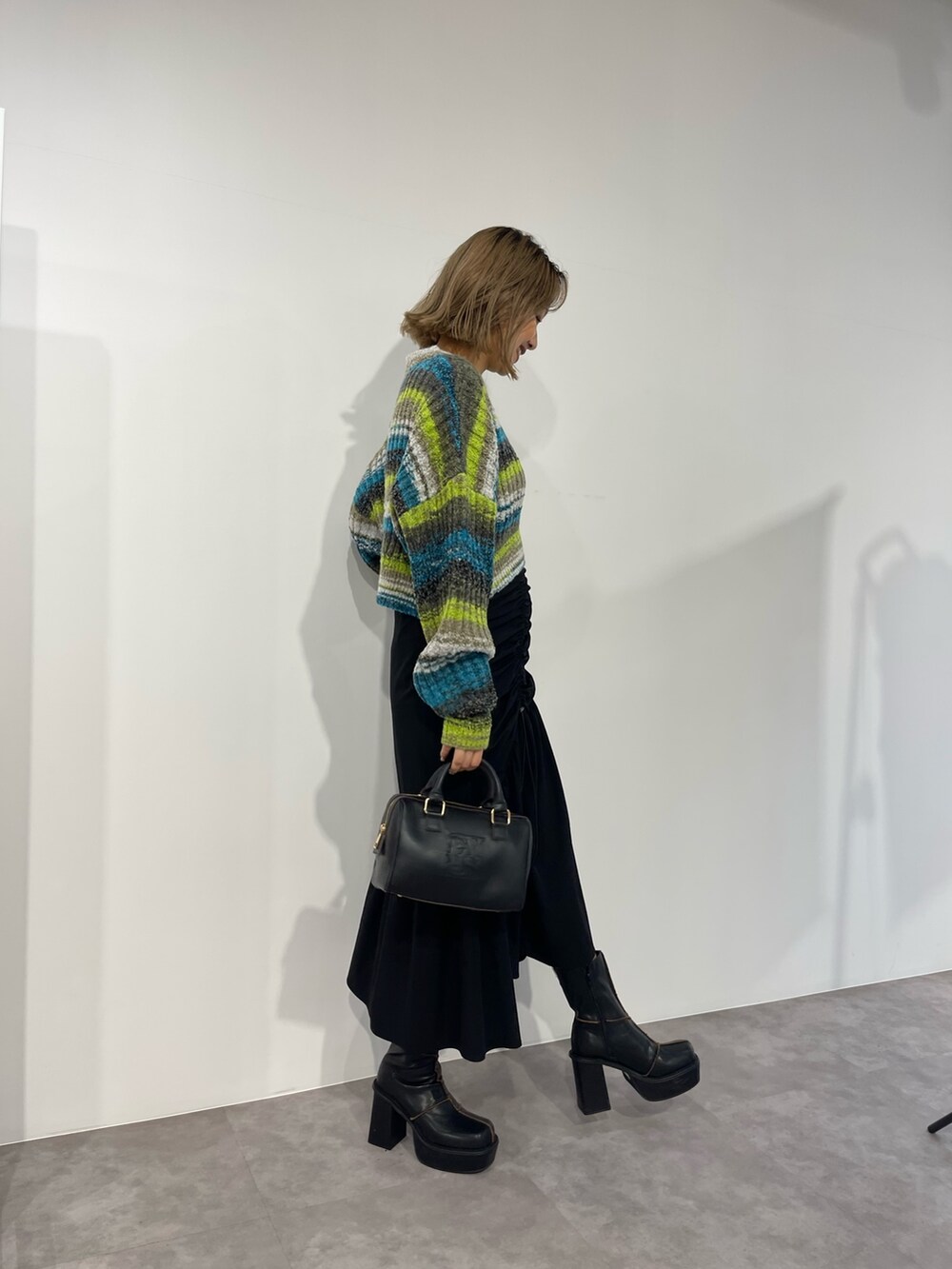 グリーン系のニット/セーター、ブラック系のボストンバッグ、ブラック系のスカートを着用したレディースの秋コーディネートの5枚目の写真