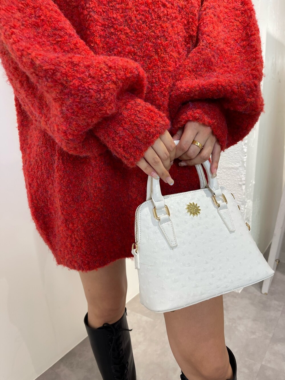 レッド系のニット/セーター、ブラック系のブーツ、ホワイト系のショルダーバッグを着用したレディースの秋コーディネートの6枚目の写真