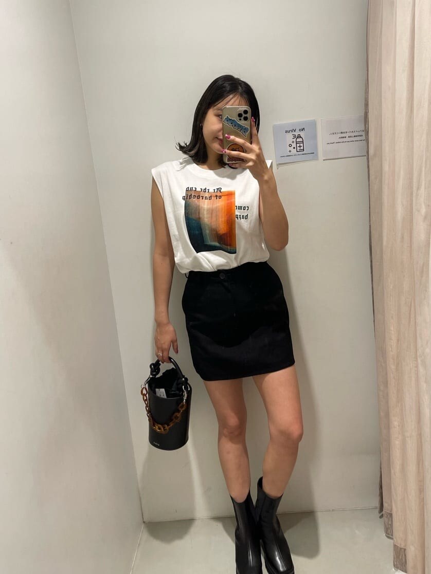 ブラック系のスカート、ホワイト系のTシャツ/カットソー、ブラック系のブーツを着用したレディースの春コーディネートの2枚目の写真