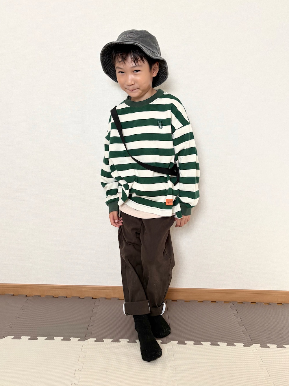 グリーン系のTシャツ/カットソー、ブラウン系のチノパンツ、ブラック系のハットを着用したキッズの秋コーディネートの4枚目の写真