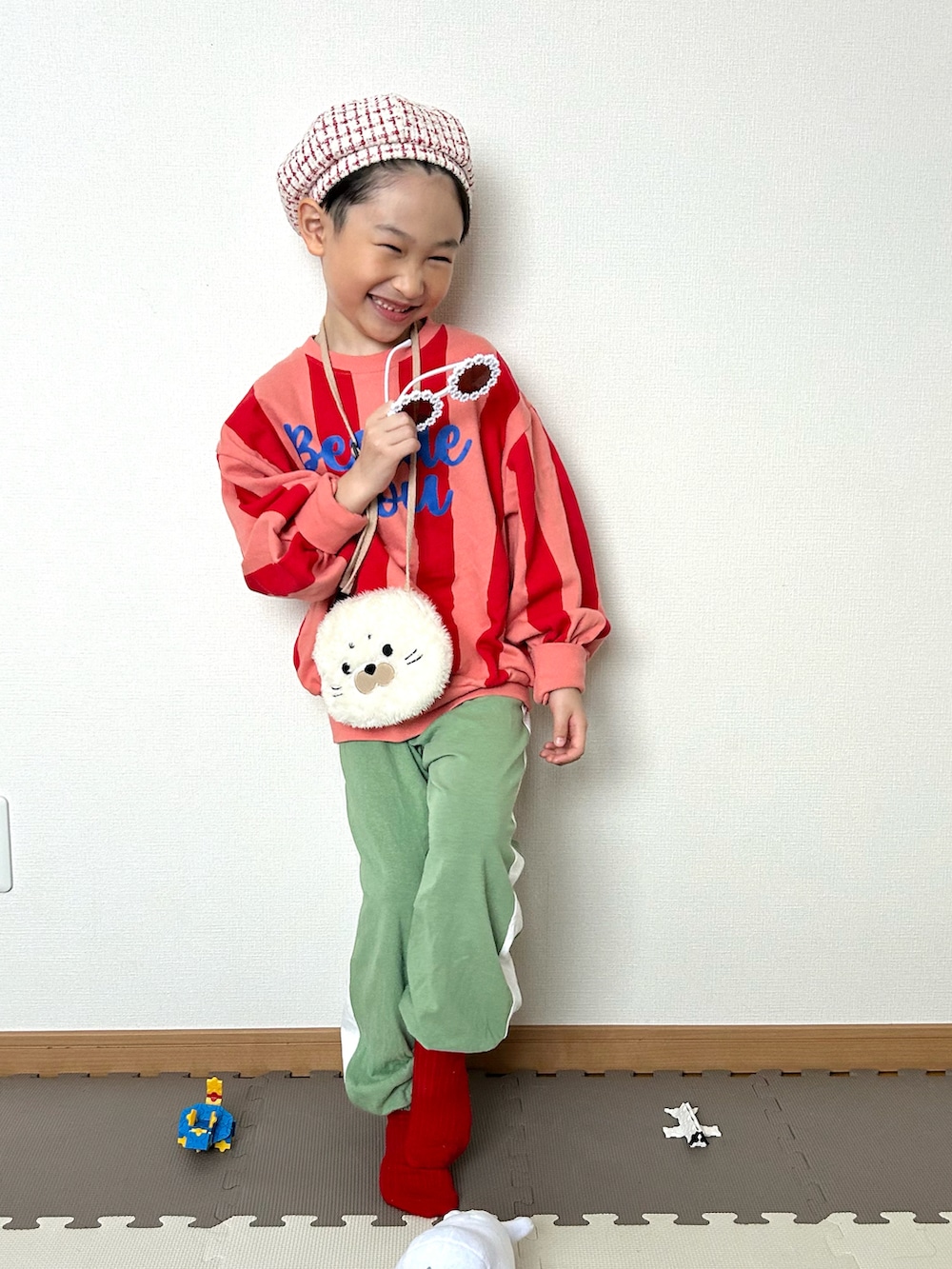 グリーン系のスウェットパンツ、ピンク系のスウェット、ホワイト系のショルダーバッグを着用したキッズの冬コーディネートの2枚目の写真