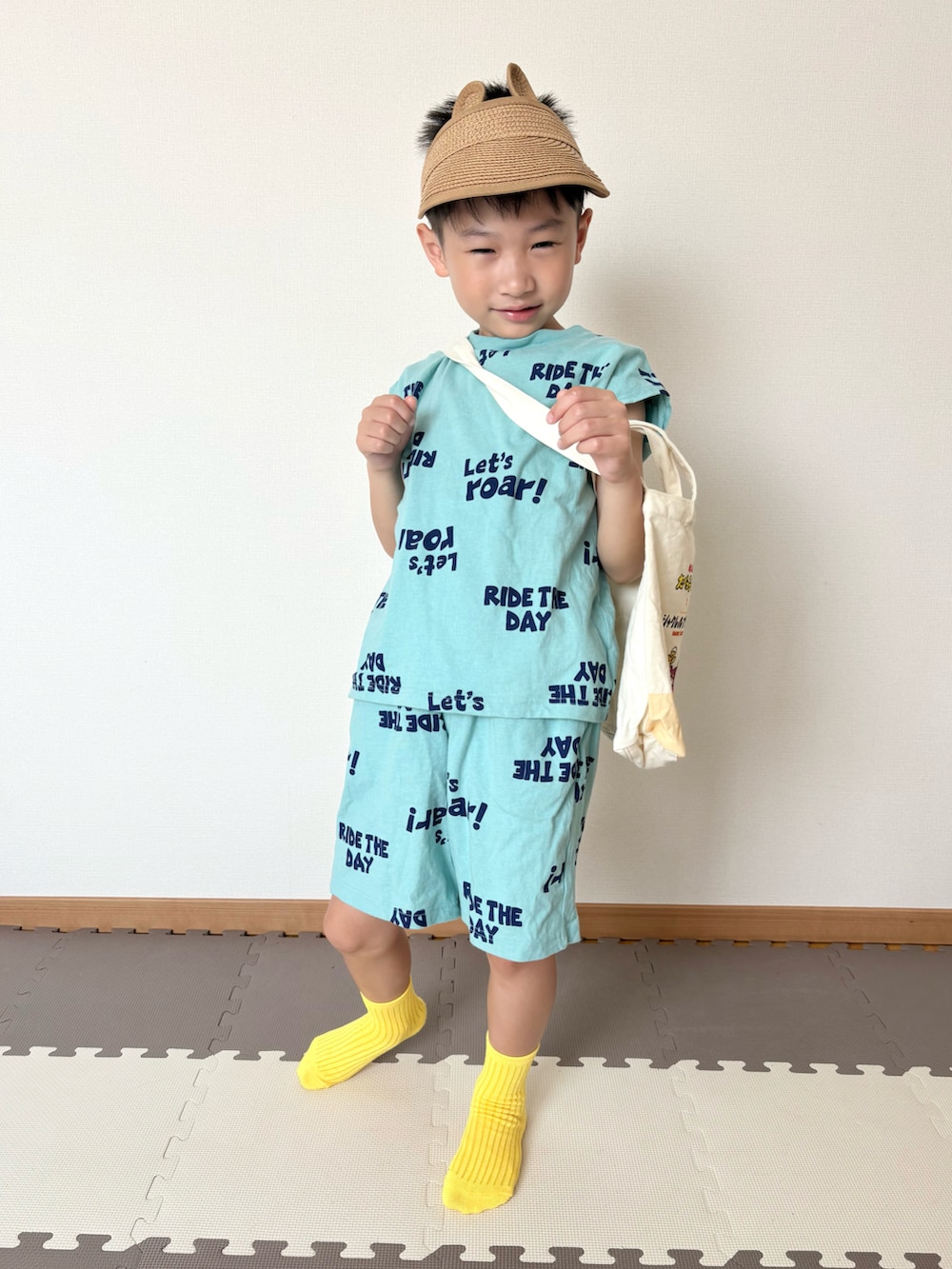 グリーン系のセットアップ、ベージュ系のトートバッグ、レッド系のおもちゃを着用したキッズの夏コーディネートの4枚目の写真
