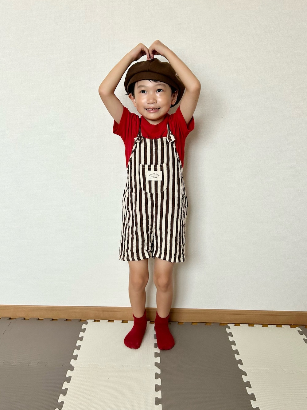 ブラウン系のサロペット/オーバーオール、レッド系のTシャツ/カットソー、ブラウン系のハンチング/ベレー帽を着用したキッズの夏コーディネートの4枚目の写真