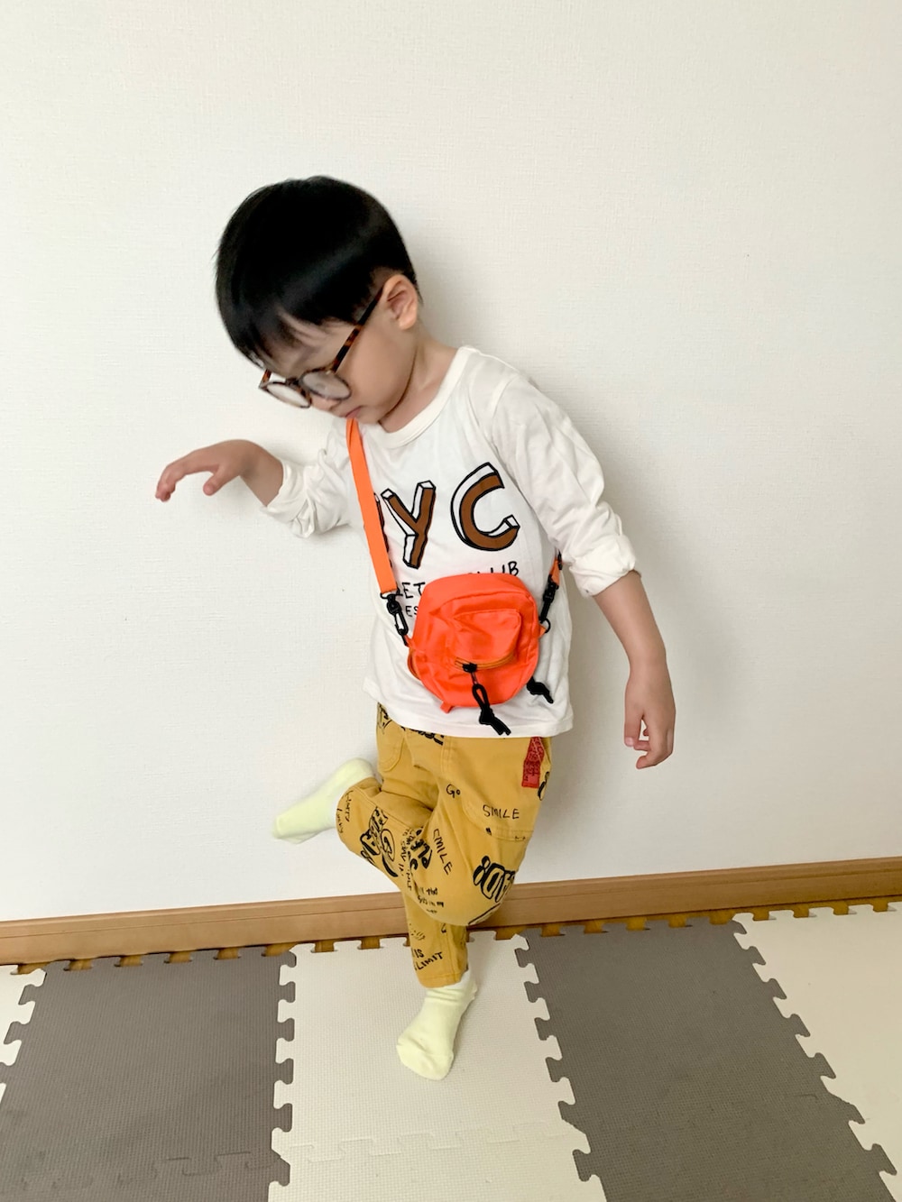 オレンジ系のショルダーバッグ、イエロー系のその他パンツ、ホワイト系のTシャツ/カットソーを着用したキッズの春コーディネートの3枚目の写真