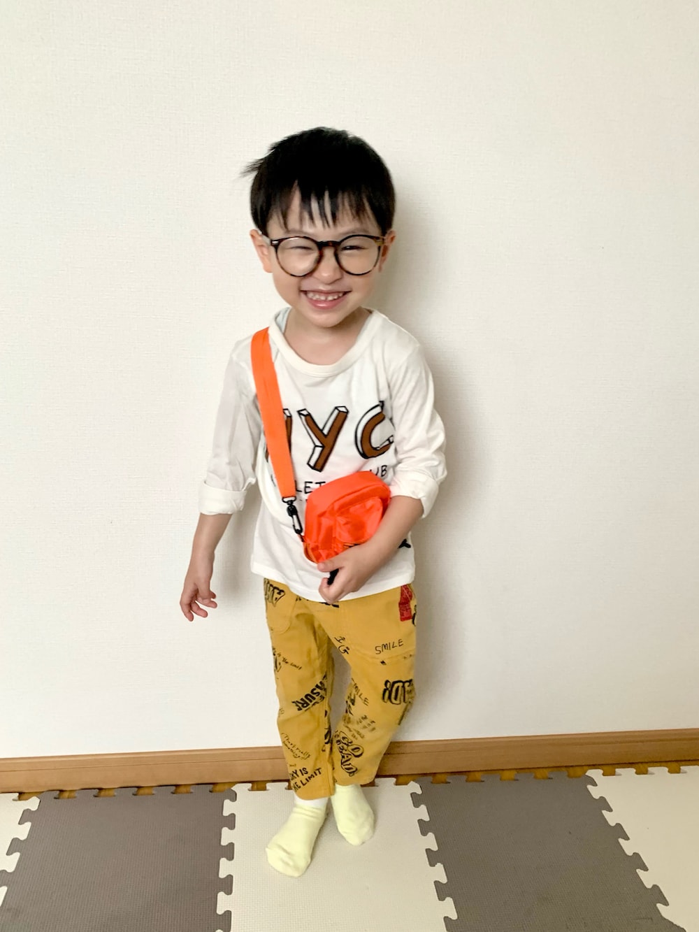 オレンジ系のショルダーバッグ、イエロー系のその他パンツ、ホワイト系のTシャツ/カットソーを着用したキッズの春コーディネートの2枚目の写真