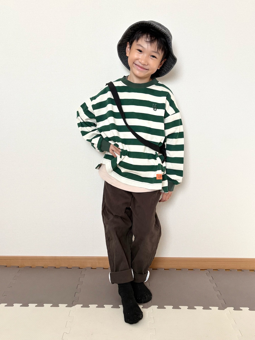 グリーン系のTシャツ/カットソー、ブラウン系のチノパンツ、ブラック系のハットを着用したキッズの秋コーディネートの5枚目の写真