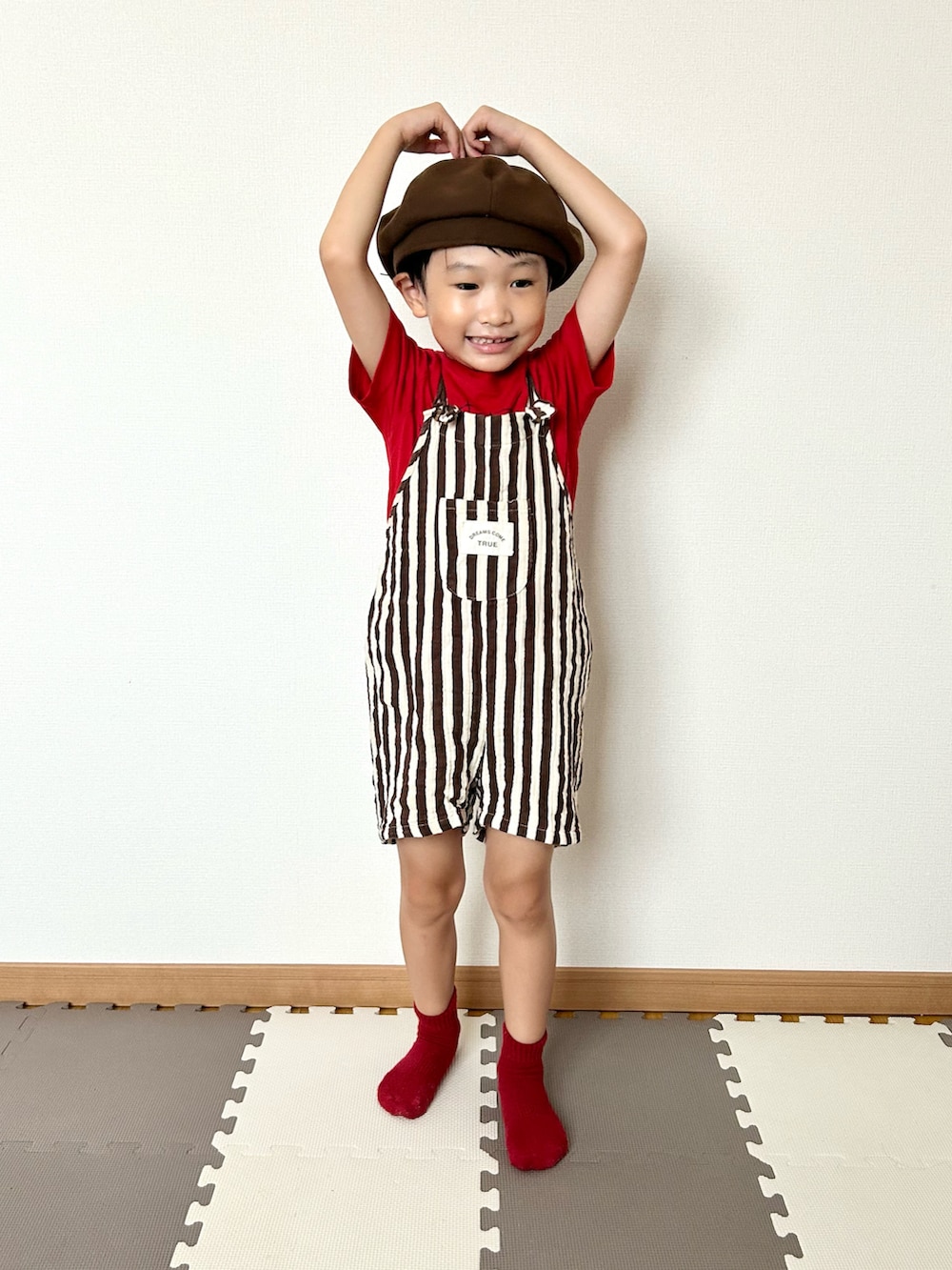 ブラウン系のサロペット/オーバーオール、レッド系のTシャツ/カットソー、ブラウン系のハンチング/ベレー帽を着用したキッズの夏コーディネートの3枚目の写真