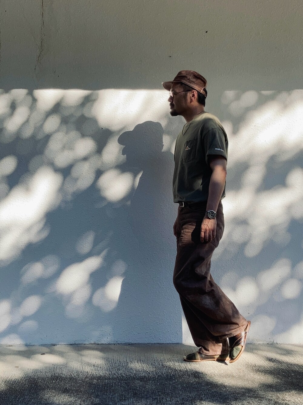 ブラウン系のデニムパンツ、グリーン系のTシャツ/カットソー、ブラウン系のサンダルを着用したメンズの夏コーディネートの3枚目の写真