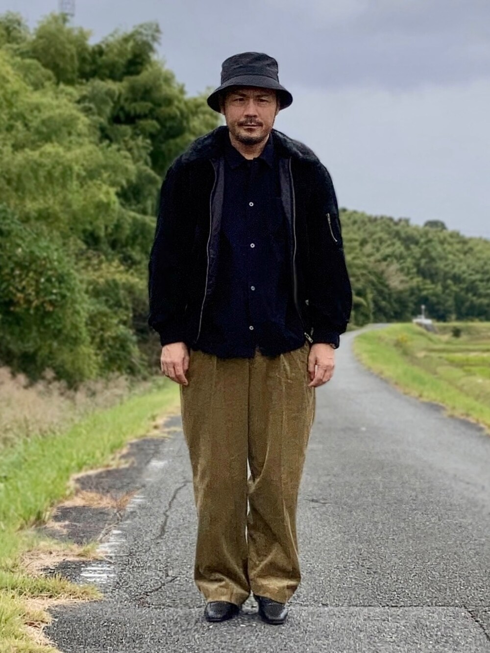 ブラック系のシャツ/ブラウス、ブラック系のブルゾン、ゴールド系のスラックスを着用したメンズの秋コーディネートの2枚目の写真