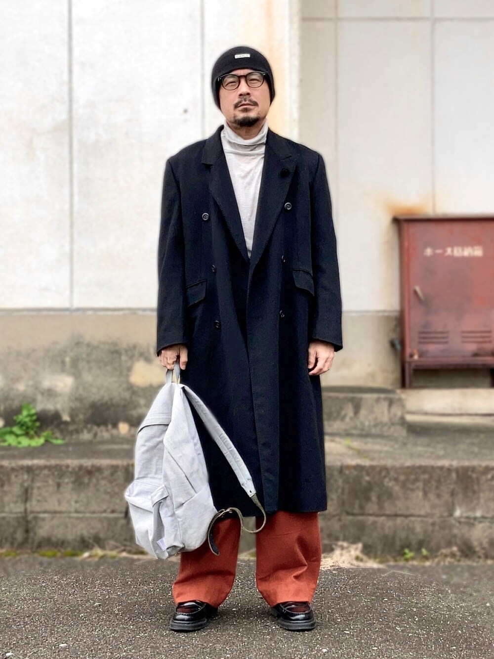 グレー系のTシャツ/カットソー、ブラック系のチェスターコート、オレンジ系のカーゴパンツを着用したメンズの冬コーディネートの2枚目の写真